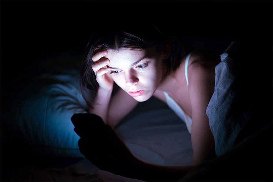 A young girl lies in bed and cannot sleep, reads and chat on social networks on a smartphone.